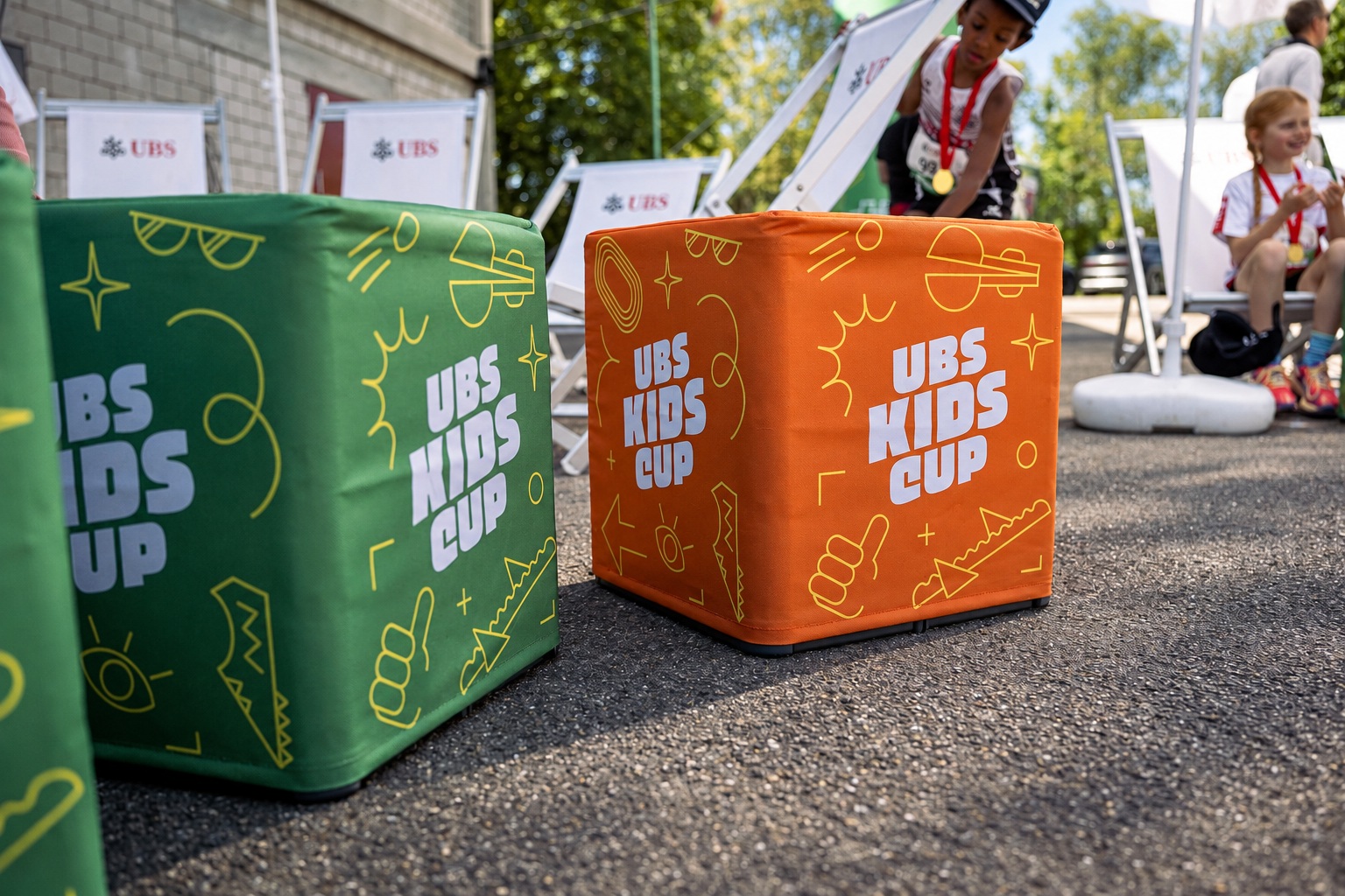 Orange-grüne Sitzwürfel des UBS Kids Cup mit Kindern im Hintergrund