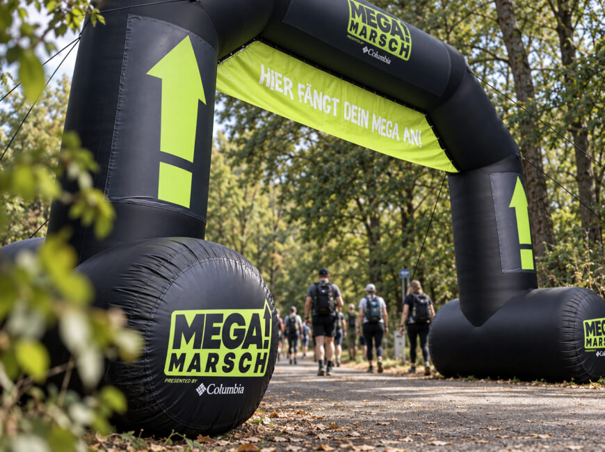 Wandernde am Megamarsch-Startbogen, aufgenommen aus niedriger Perspektive